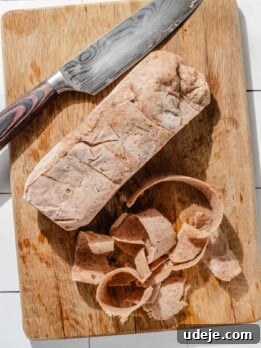 One-Pan Lamb and Beef Doner Kebab 24 Frozen doner log being cut into thin slices with a large knife on a wooden cutting board