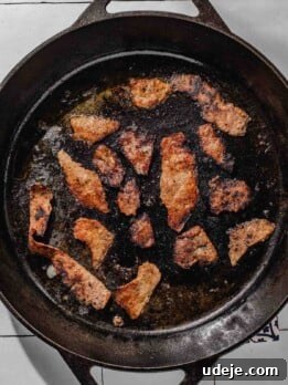 One-Pan Lamb and Beef Doner Kebab 25 Cast iron skillet with doner slices being fried on a white tiled background
