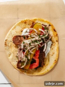 One-Pan Lamb and Beef Doner Kebab 26 Pita with doner meat and toppings (pickles, sliced onions, tomato) on a brown parchment paper on a white tiled background