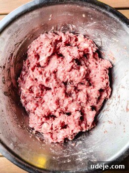 Raw ground meat mixture for Iraqi Kabab in a large metal bowl, seen from above. The pink, slightly marbled meat is ready to be shaped and cooked. The bowl rests on a wooden surface.