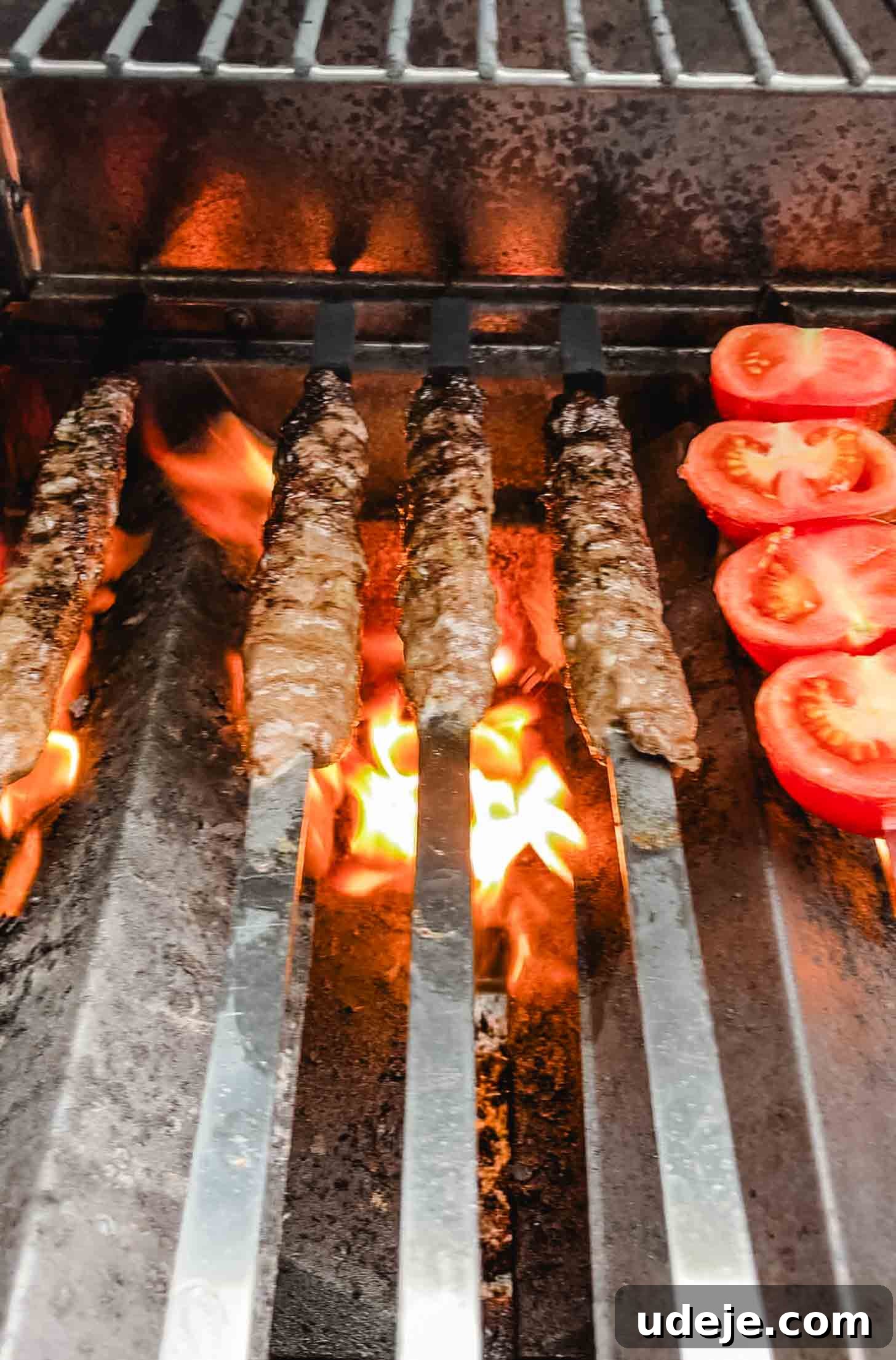 Sizzling Iraqi Kabab A Taste of Tradition 8 Iraqi kabab on flat metal skewers being grilled over an open flame, along with a skewer of tomatoes, showcasing the direct heat cooking method.