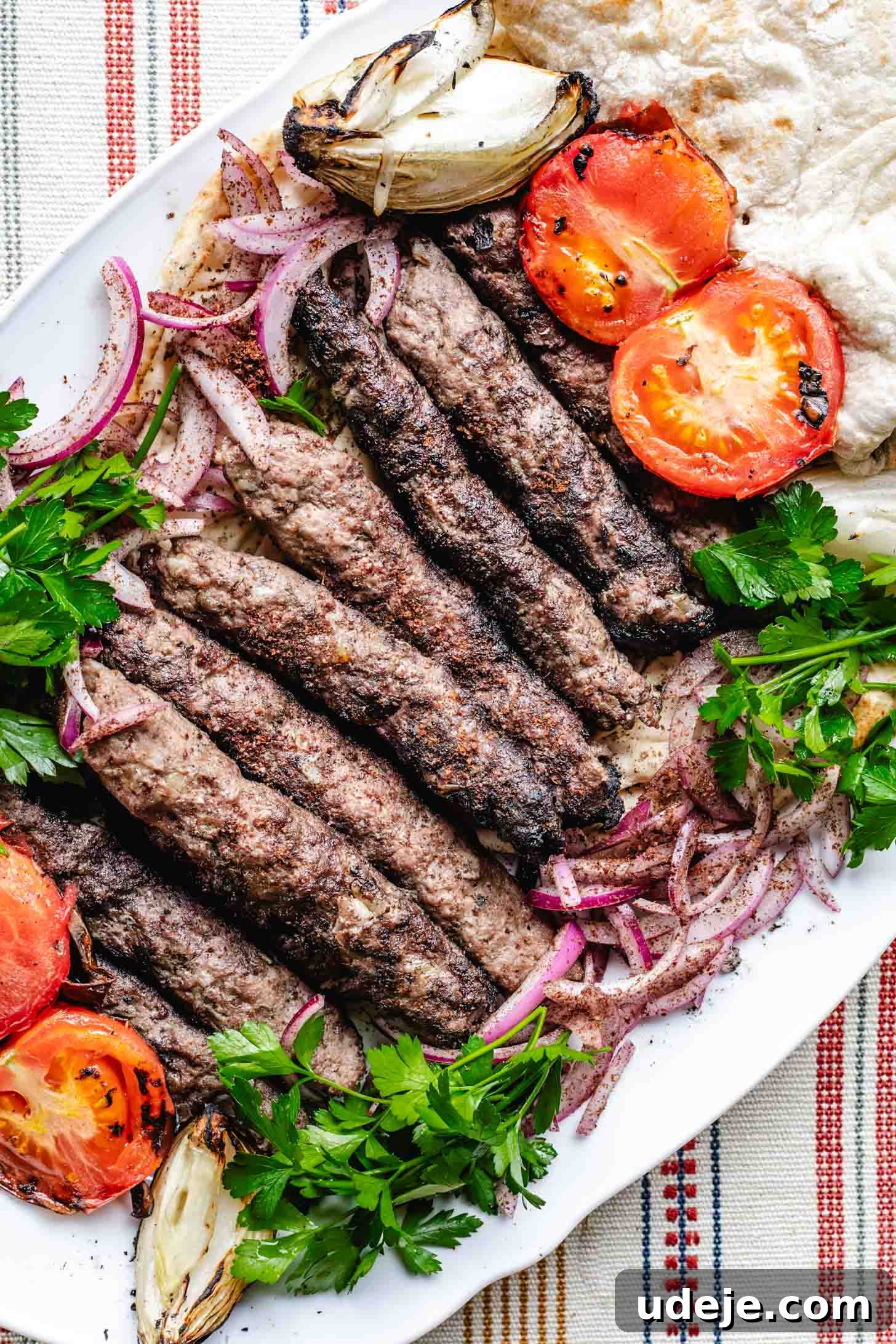 Sizzling Iraqi Kabab A Taste of Tradition 9 Grilled Iraqi kabab skewers are plated on a large white platter, along with sumac onions, parsley, grilled tomato, grilled onions and Iraqi bread, artfully arranged for serving.