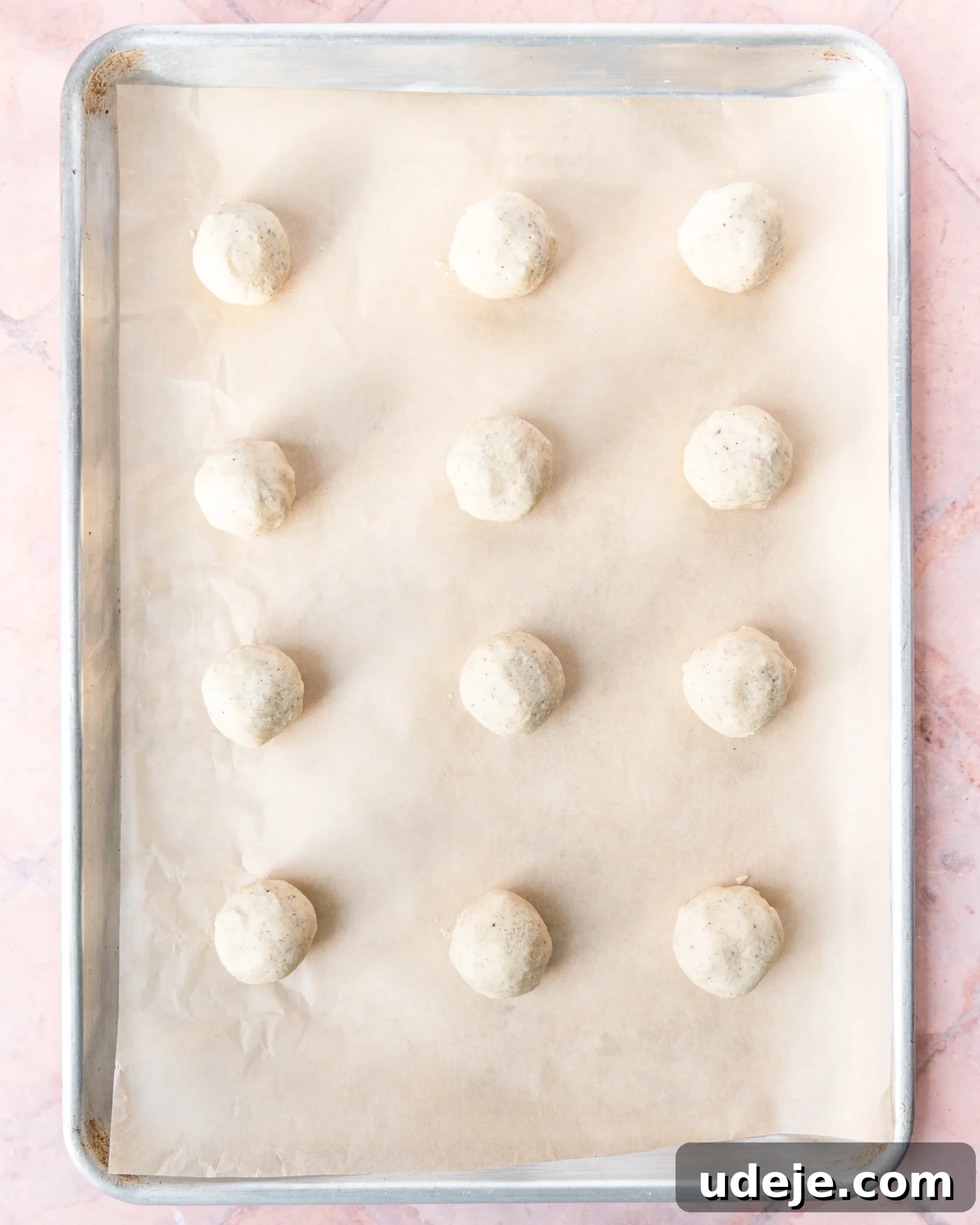 Fragrant Cardamom Shortbread Cookies 11 Baking sheet lined with parchment with 12 evenly spaced dough balls on a light red tiled background.