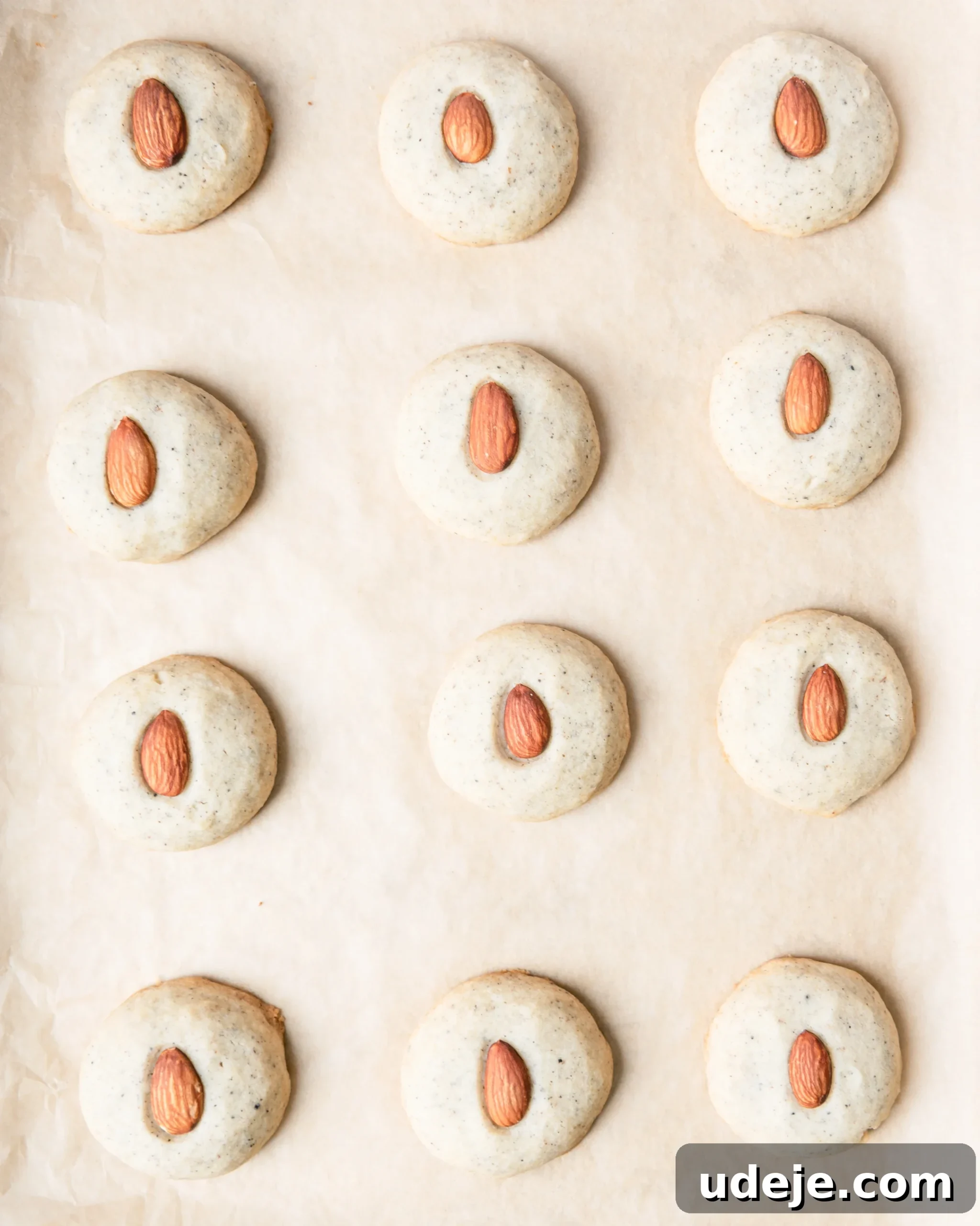 Fragrant Cardamom Shortbread Cookies 14 Baked shortbread cookies with an almond in the centre on parchment paper.
