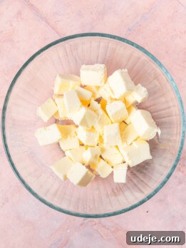 Cubed butter in a glass bowl on a light red tiled background.