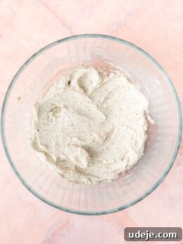 Creamed butter with cardamom and baking powder in a glass bowl on a light red tiled background.