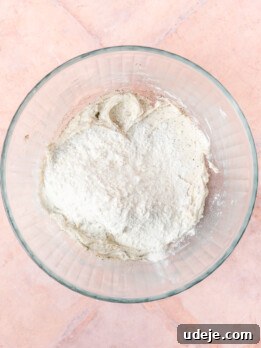 Creamed butter with cardamom and baking powder in a glass bowl with flour on a light red tiled background.