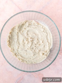 Cardamom shortbread dough in a glass bowl on light red tiled background.