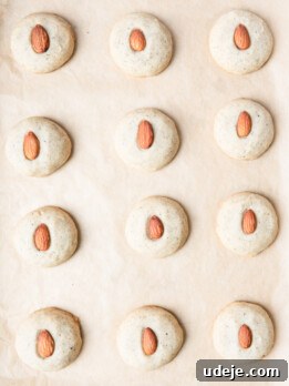 Baked shortbread cookies with an almond in the centre on parchment paper.