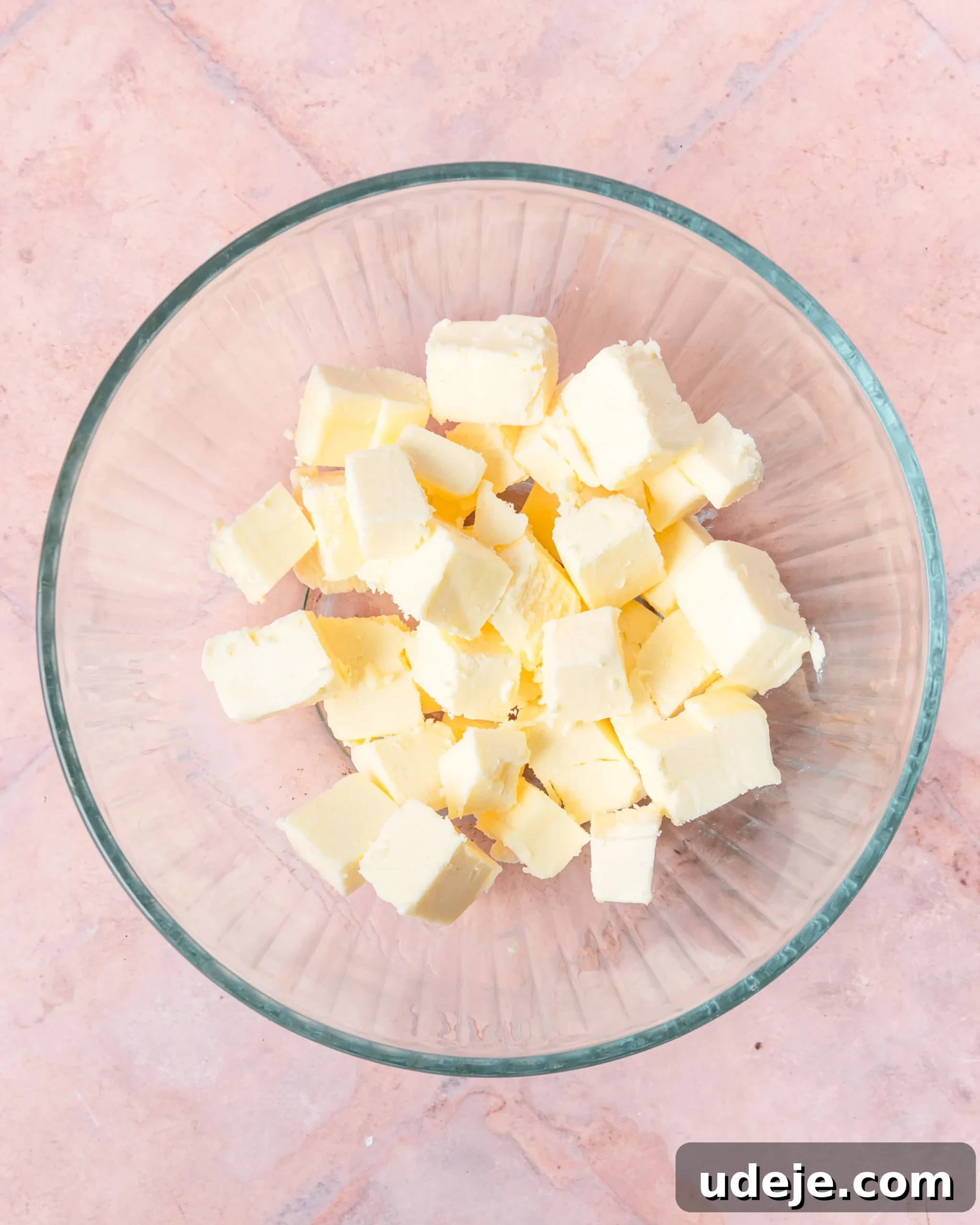 Fragrant Cardamom Shortbread Cookies 4 Cubed butter in a glass bowl on a light red tiled background.
