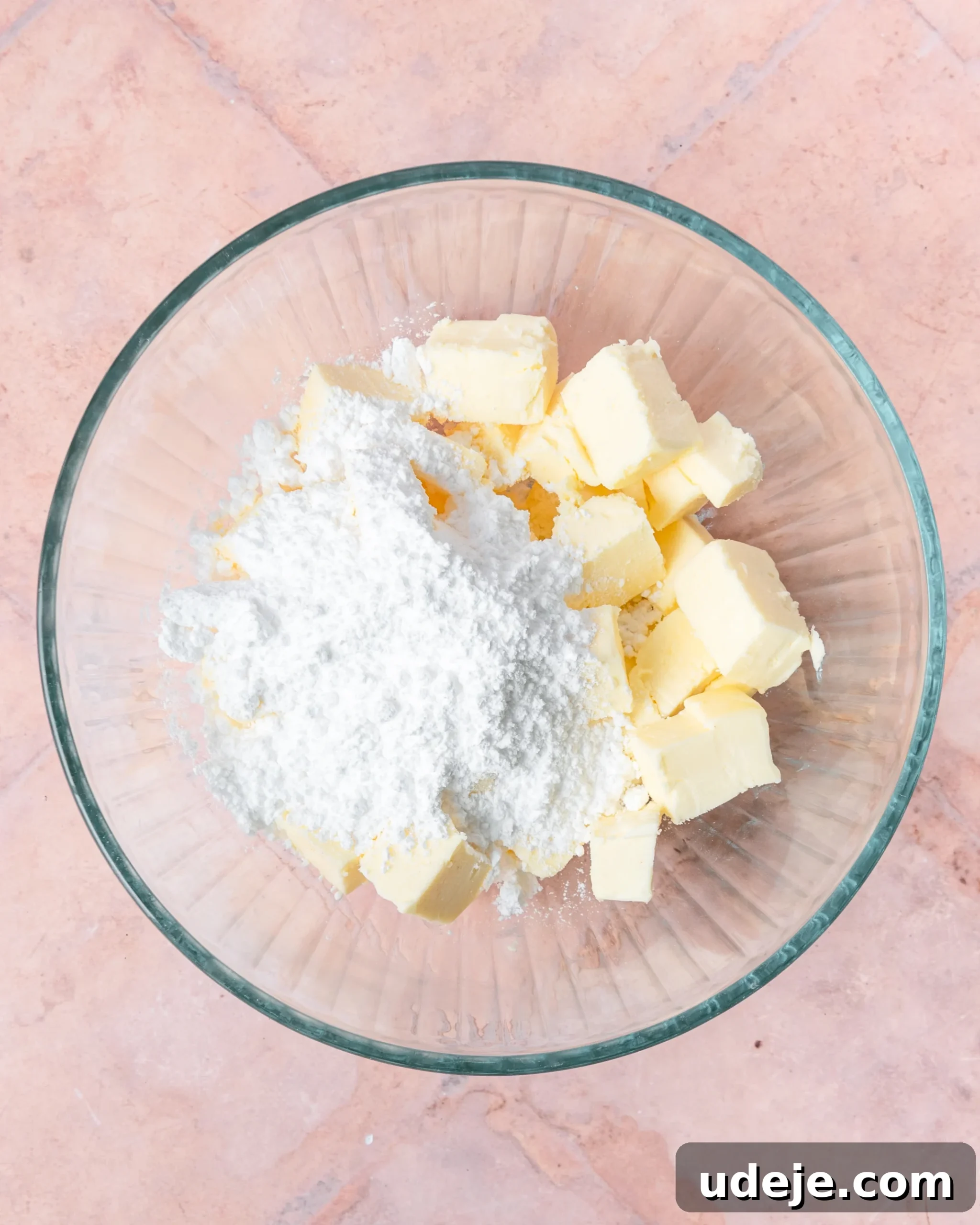 Fragrant Cardamom Shortbread Cookies 5 Glass bowl with cubed butter and powdered sugar on a light red tiled background.