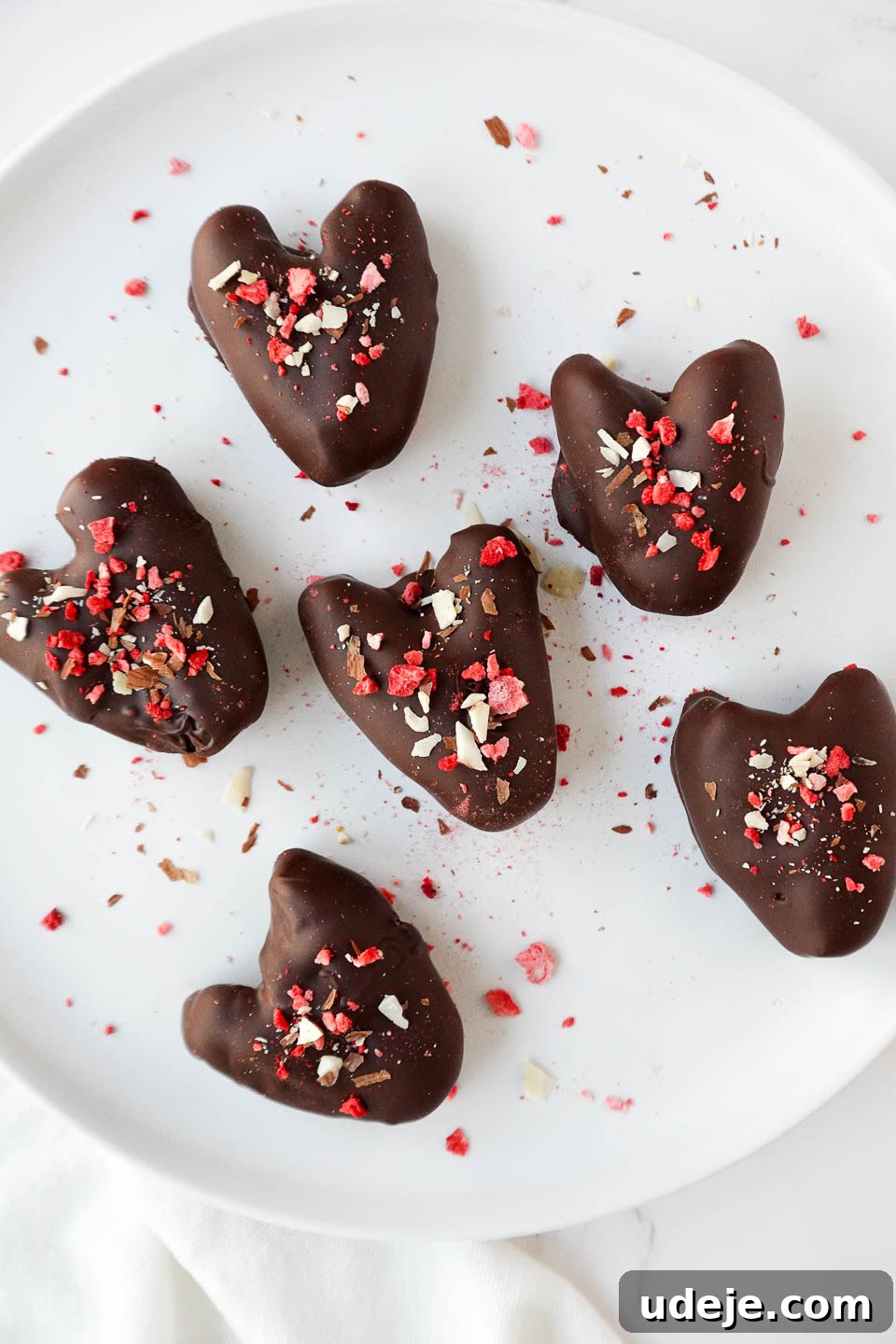 Decadent Chocolate Date Gems 4 Heart-shaped Medjool dates stuffed with peanut butter and coated in dark chocolate, topped with freeze-dried strawberries, chopped nuts, and flaky sea salt. These chocolate date hearts are the perfect healthy Valentine's Day treat!