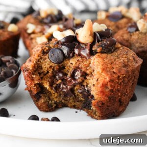 Moist and tender healthy banana muffins on a plate with a bite taken out showing gooey chocolate chips and it's fluffy, moist texture