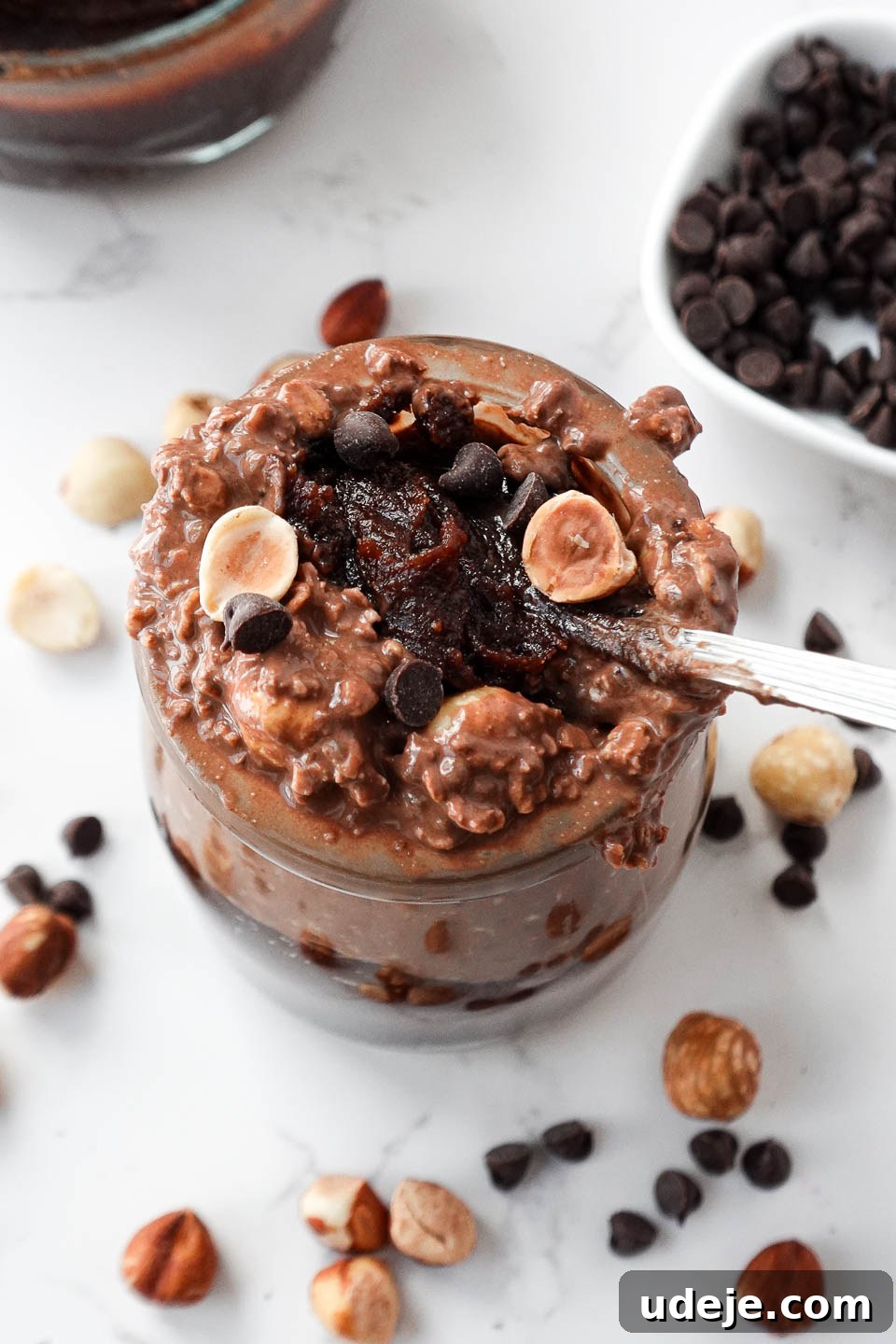 Dreamy Chocolate Hazelnut Overnight Delight 2 A spoon scooping up thick and creamy vegan chocolate hazelnut overnight oats with dark chocolate chips and hazelnuts on top and a spoonful of homemade healthy nutella