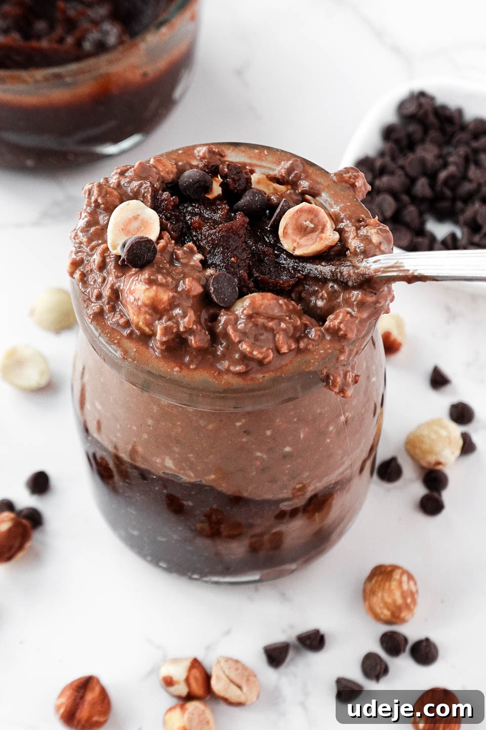 Dreamy Chocolate Hazelnut Overnight Delight 4 A glass jar filled with creamy chocolate hazelnut overnight oats, topped with chopped hazelnuts and a spoonful of homemade Nutella
