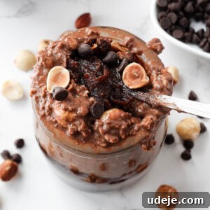 A spoon scooping up thick and creamy vegan chocolate hazelnut overnight oats with dark chocolate chips and hazelnuts on top and a spoonful of homemade healthy nutella
