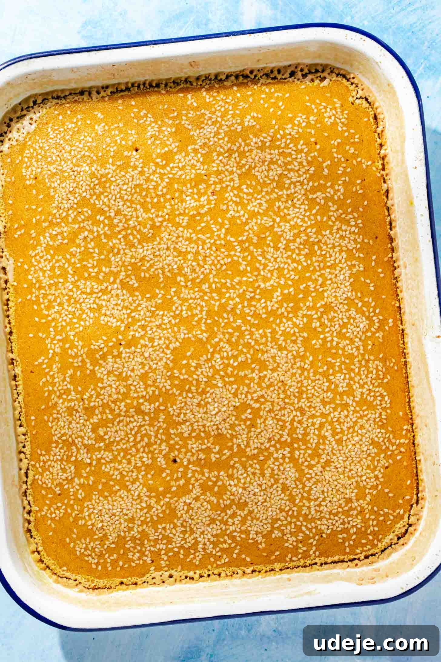 Aromatic Golden Semolina Cake 9 Freshly baked golden yellow Sfouf cake in a white rectangular baking pan with a blue rim, resting on a blue background.