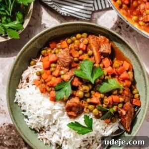 Veal stew with peas and carrots in a green bowl with white rice and parsley on top with a fork, with a white pot of it at the side, a white and black striped tea towel and a small bowl of parsley on a beige marble background.
