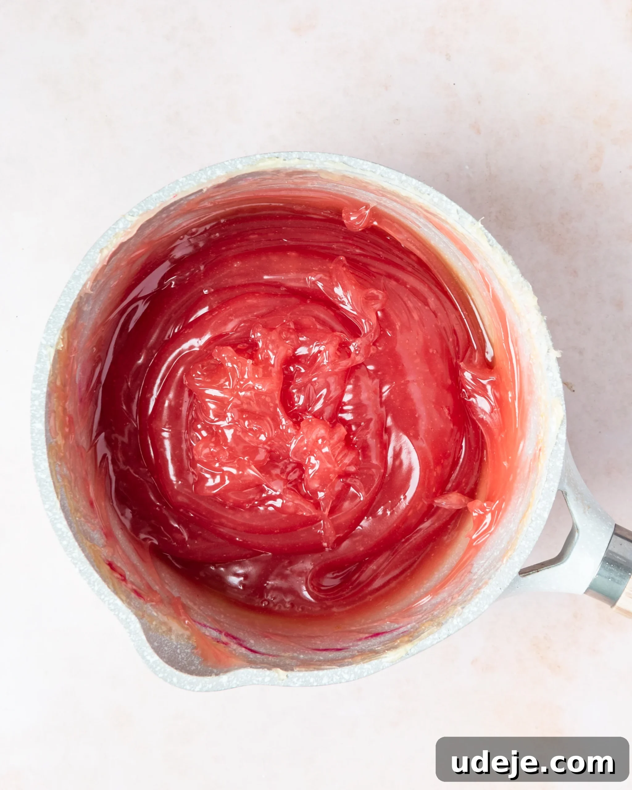 Homemade Turkish Delight: Customize with Pistachios 14 A vibrantly gelled red mixture, now infused with food coloring, in a small light grey saucepan on a soft pink background.