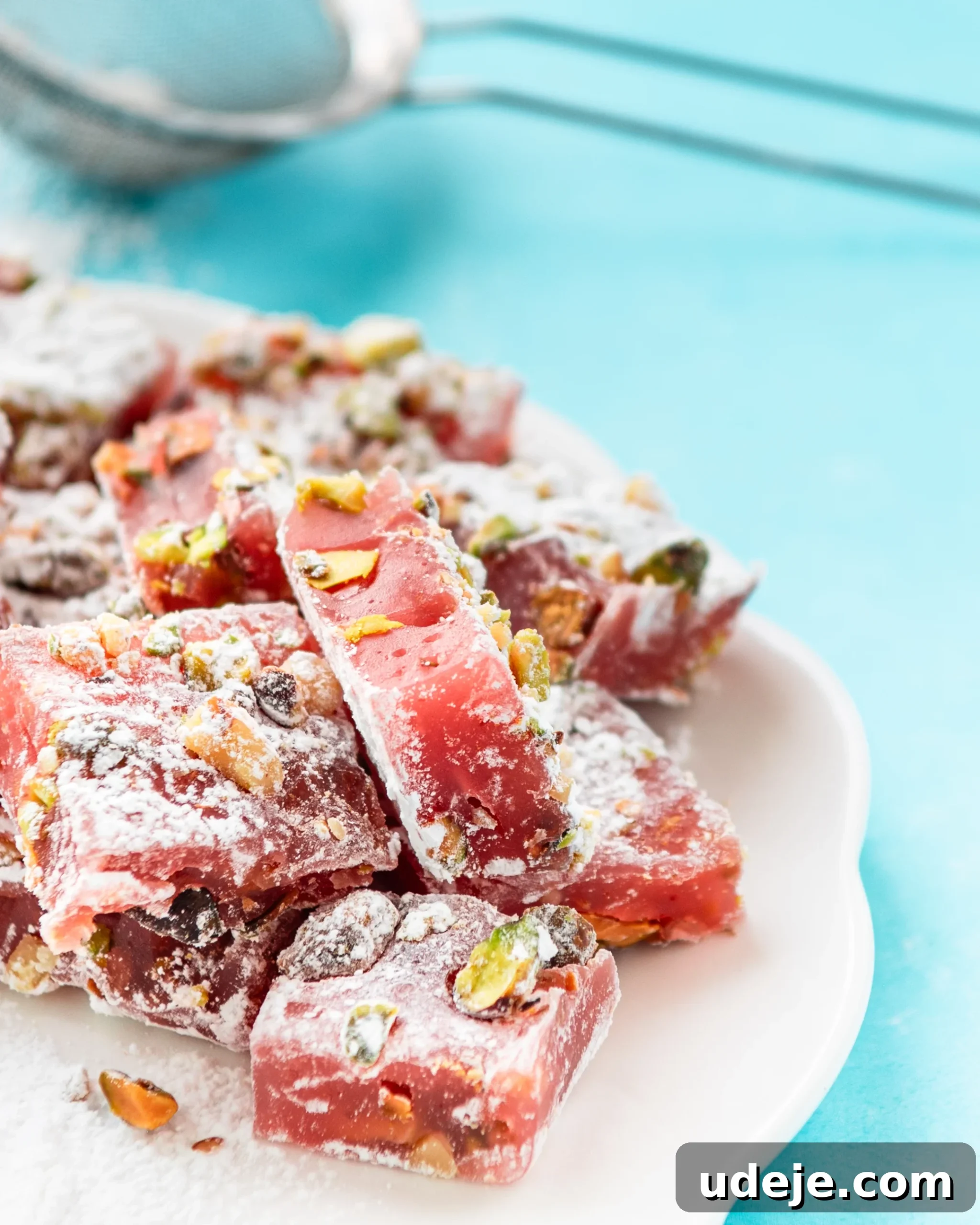 Homemade Turkish Delight: Customize with Pistachios 22 Perfectly cut squares of Turkish Delight, elegantly stacked on a white plate with a subtle blue background, exuding an inviting sweetness.