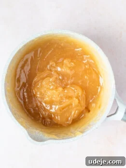 Gelled medium brown mixture in a light grey small saucepan on a soft pink background.