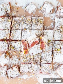 Powdered sugar on a piece of light brown parchment paper with the set turkish delight on top with powdered sugar dusted on top and cut into squares on a light pink background.