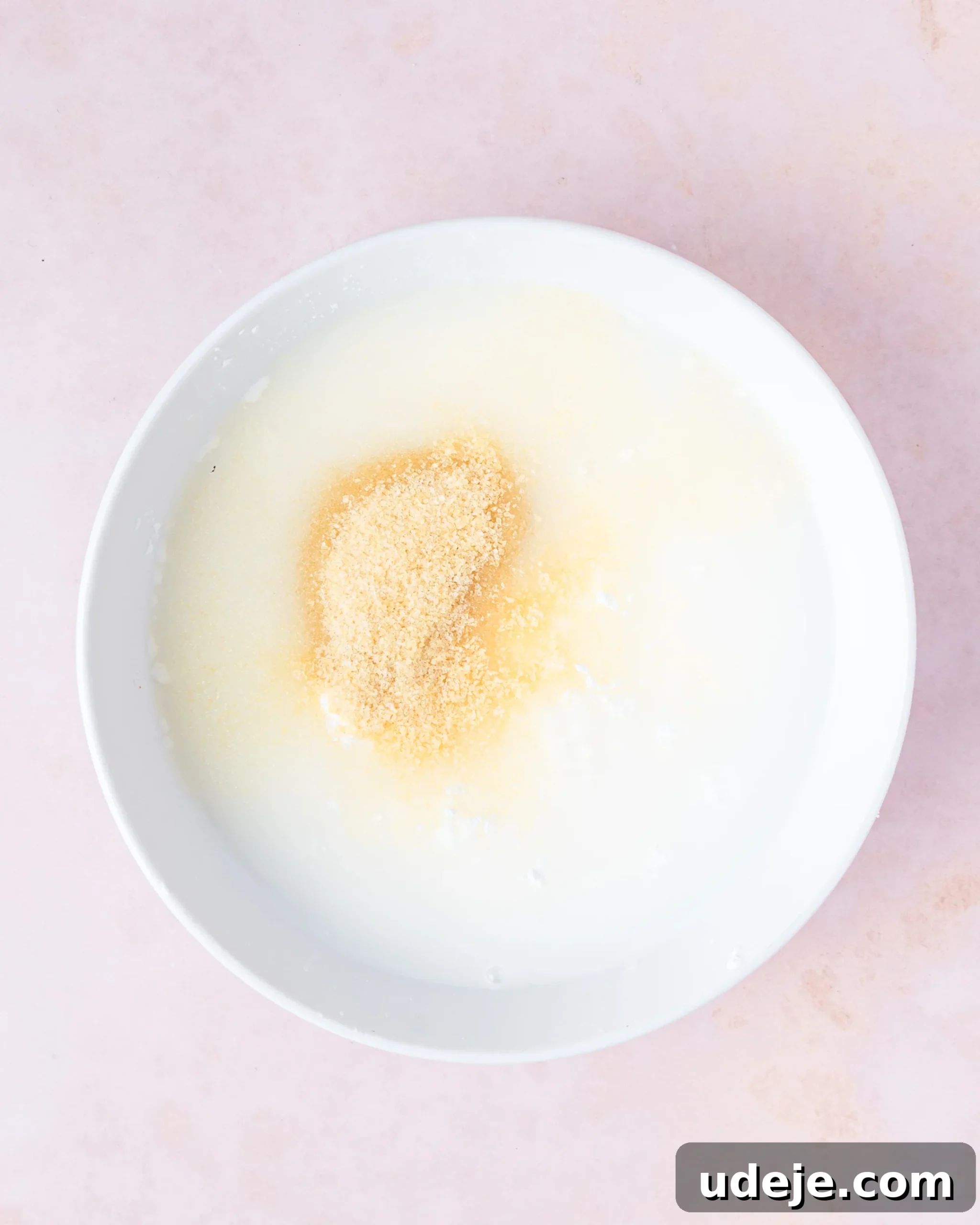 Homemade Turkish Delight: Customize with Pistachios 8 A white bowl containing water, cornstarch, and gelatin granules, ready to be mixed, on a soft pink background.