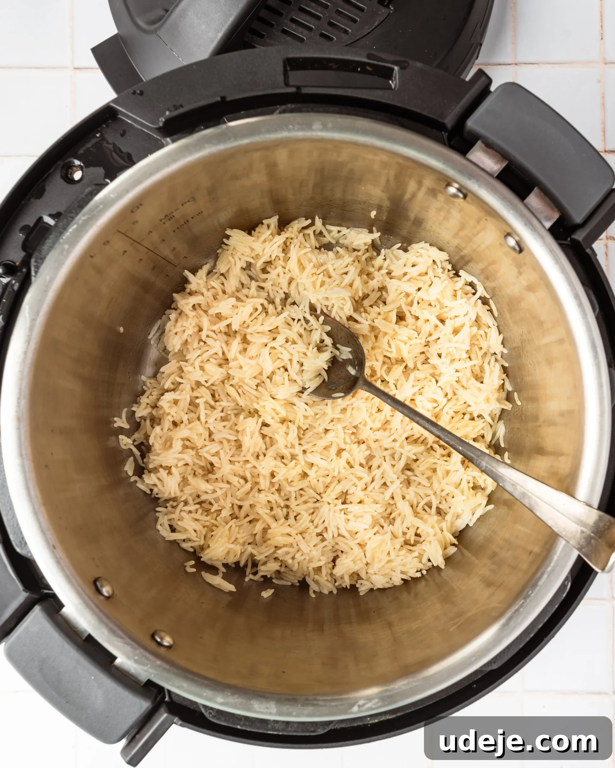 Instant Pot Basmati: Fluffy Perfection in 15 Minutes 11 Fluffy, cooked basmati rice in the Instant Pot with a serving spoon gently separating the grains, ready for the final resting step, set on a white tiled background.