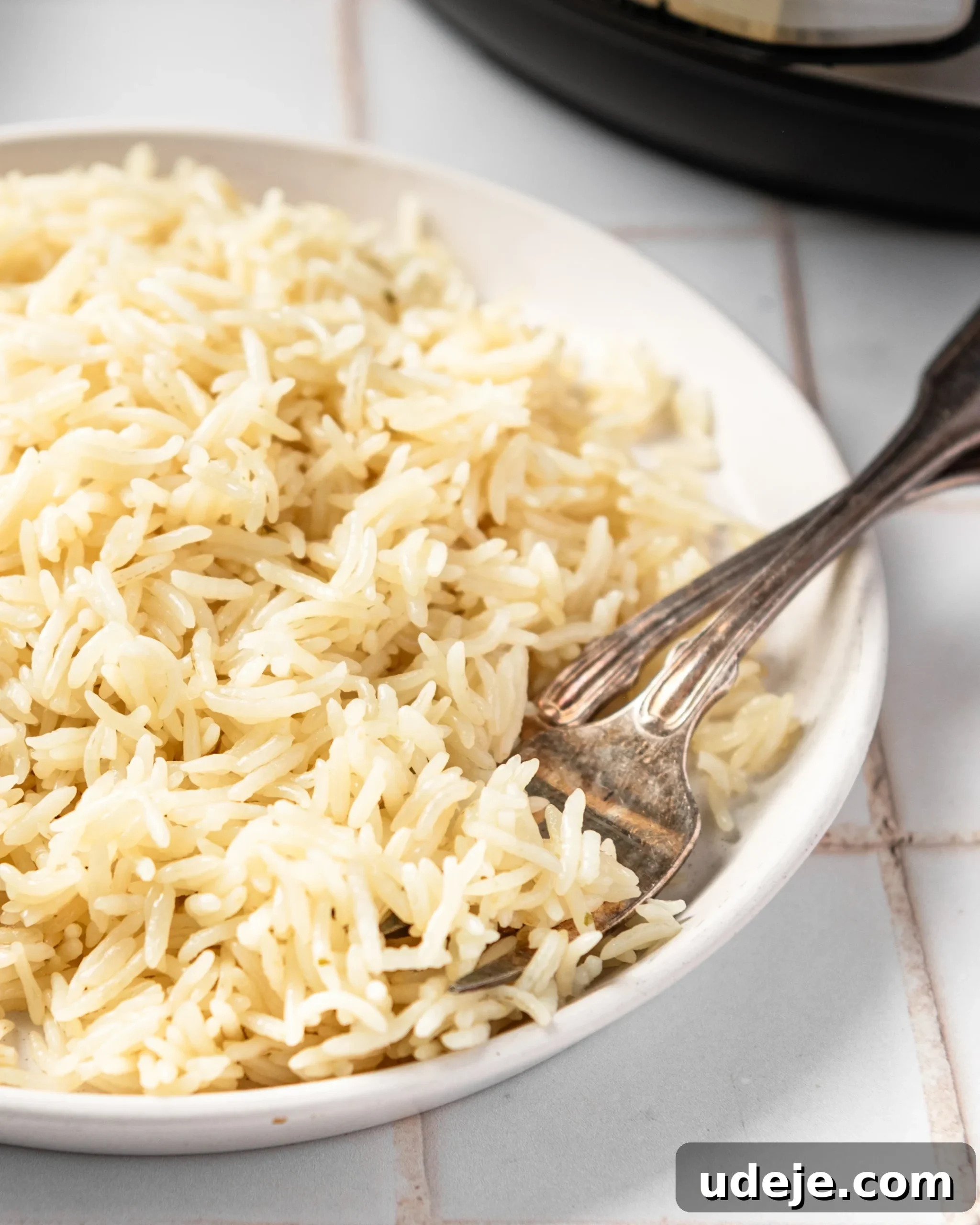 Instant Pot Basmati: Fluffy Perfection in 15 Minutes 13 Perfectly cooked basmati rice on a white plate with two forks, ready to be enjoyed, with an Instant Pot softly blurred in the background on a white tiled surface. The scene emphasizes the ease and delicious outcome of the Instant Pot cooking method.