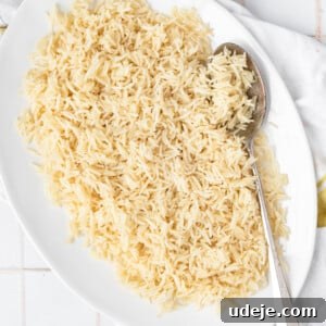 Instant Pot Basmati: Fluffy Perfection in 15 Minutes 14 Rice in a white platter with a spoon on a white and yellow tea towel with small plates and forks at the side on a white tiled background.