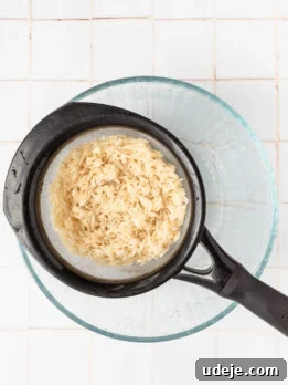 Instant Pot Basmati: Fluffy Perfection in 15 Minutes 15 Strainer with rice in it over a glass bowl on a white tiled background.