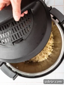 Instant Pot Basmati: Fluffy Perfection in 15 Minutes 17 Cooked rice in the insant pot with the lid on halfway on a white tiled background.