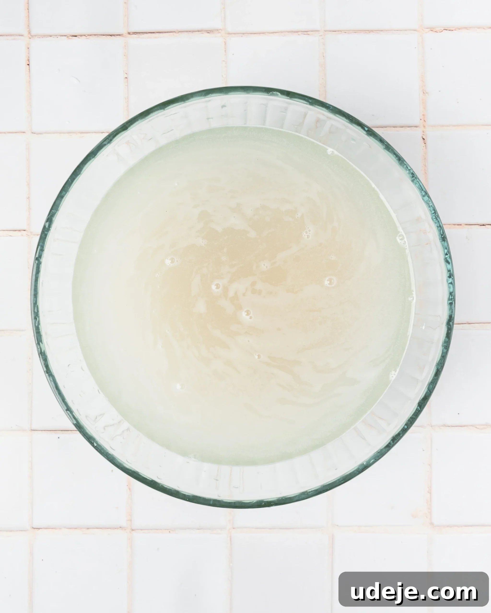 Instant Pot Basmati: Fluffy Perfection in 15 Minutes 4 Glass bowl containing basmati rice submerged in cloudy, starchy water, illustrating the initial rinsing stage, set on a clean white tiled background.