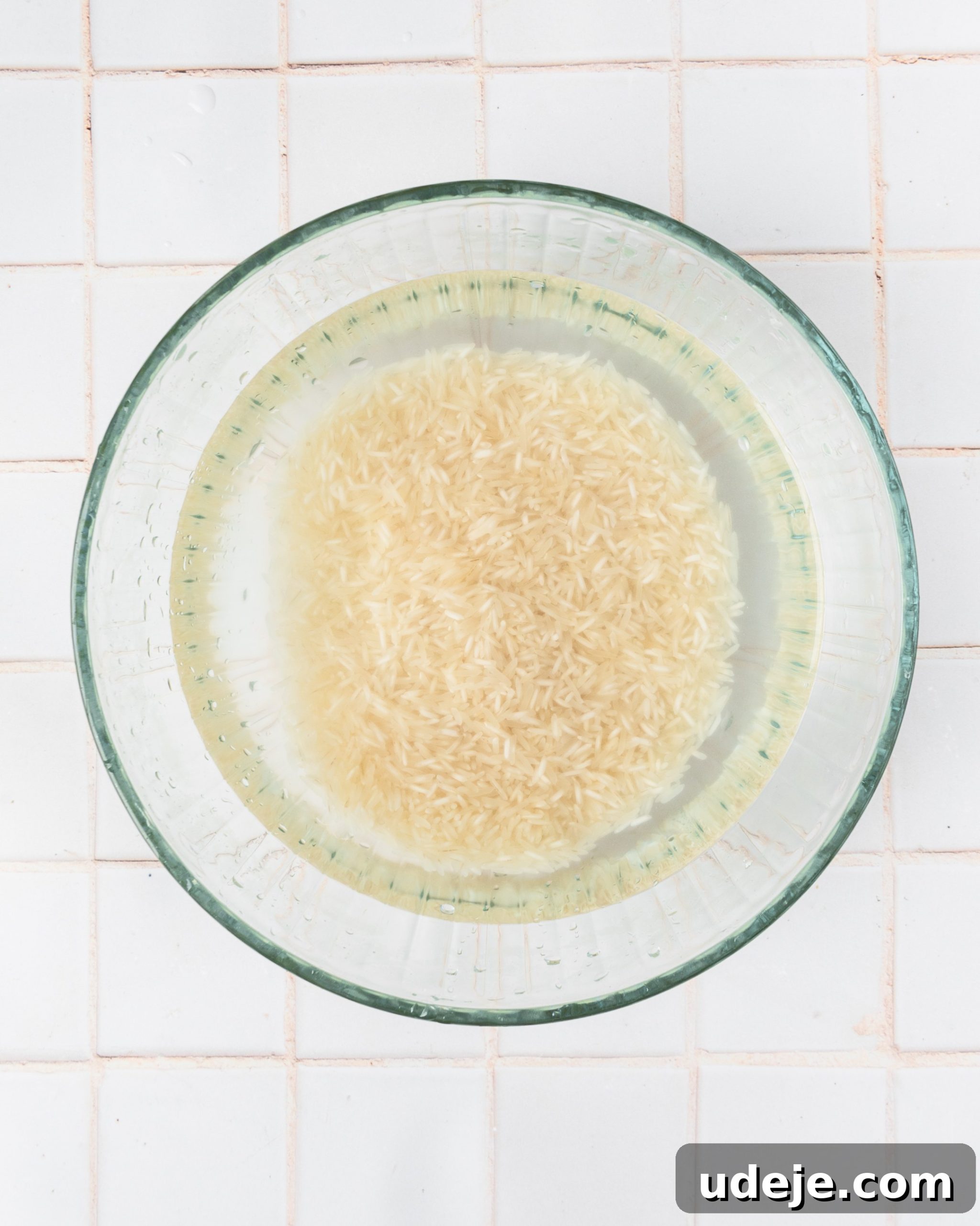 Instant Pot Basmati: Fluffy Perfection in 15 Minutes 5 Glass bowl containing basmati rice with perfectly clear water, demonstrating the completion of the rinsing process, positioned on a white tiled background.