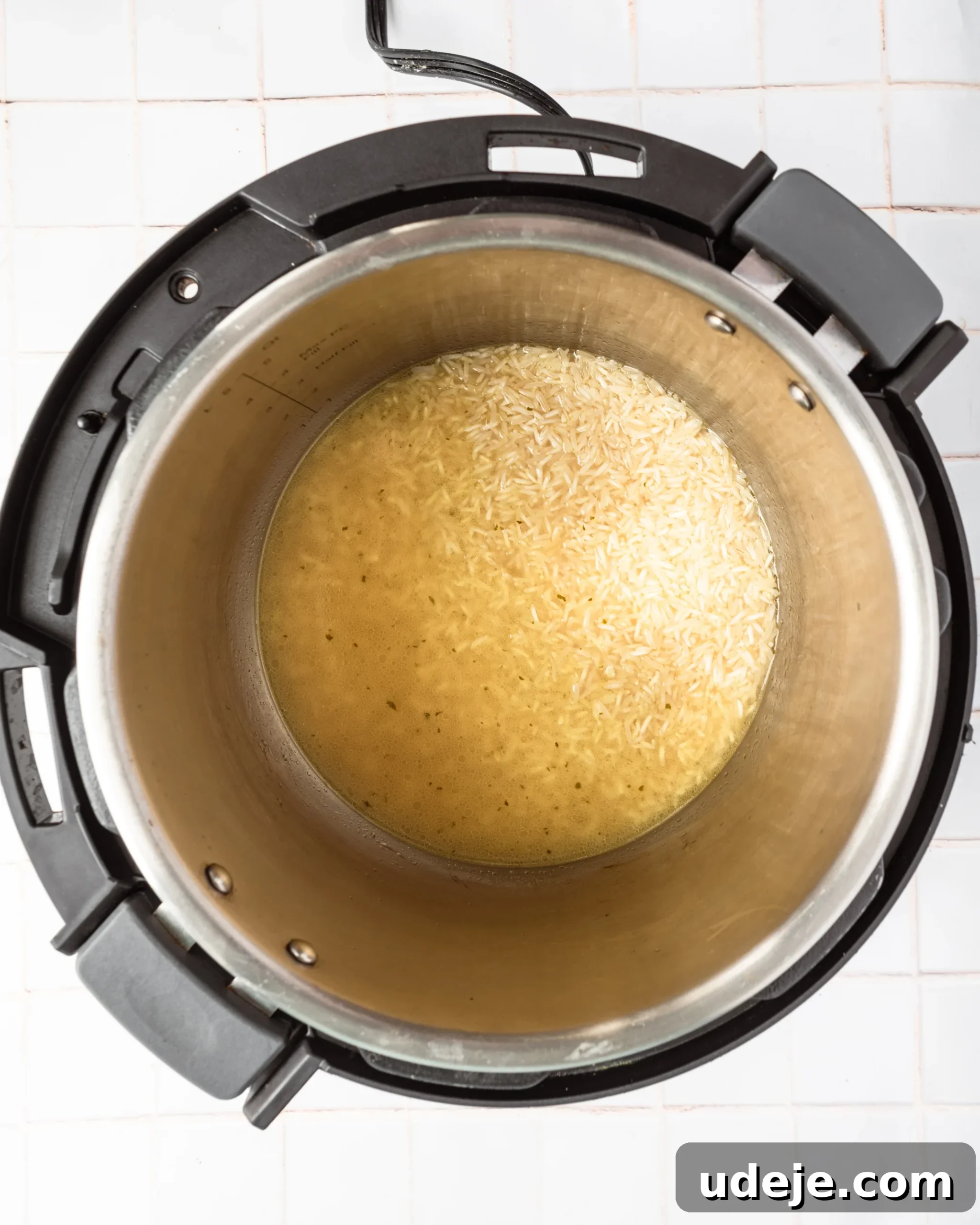 Instant Pot Basmati: Fluffy Perfection in 15 Minutes 8 Instant Pot interior with basmati rice, hot broth, and seasoning before pressure cooking, showing the readiness for the cooking phase on a white tiled background.