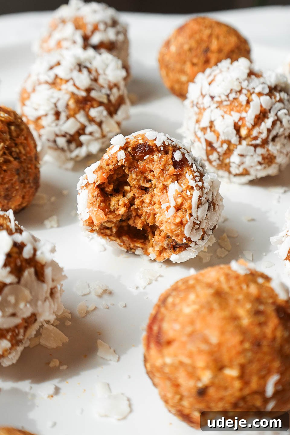 Carrot Cake Power Bites 2 A vegan carrot cake energy ball with a bite taken out, showing its chewy, spiced interior, rolled in shredded coconut.