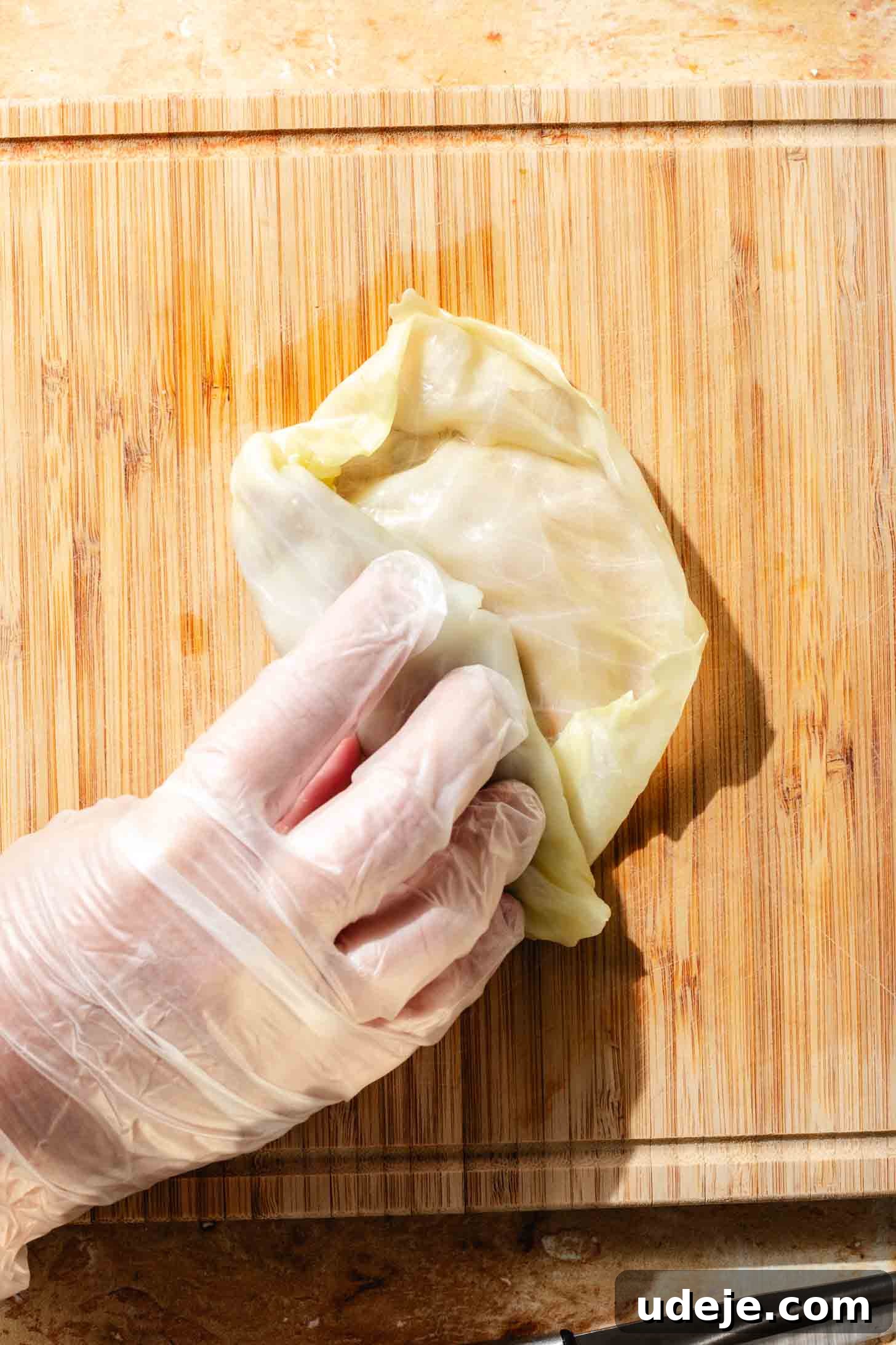 Irresistible Beef and Rice Cabbage Rolls 11 A blanched cabbage leaf, with the ground beef mixture securely tucked inside, being rolled further by a gloved hand on a light wooden background, demonstrating the rolling technique.