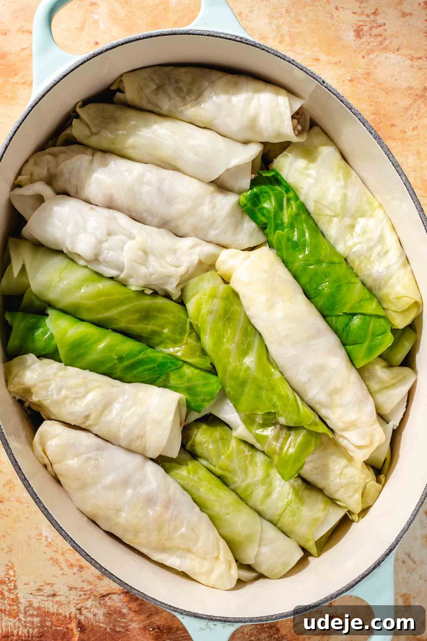 Irresistible Beef and Rice Cabbage Rolls 13 Numerous blanched and stuffed cabbage leaves, expertly rolled, are tightly arranged in an oval light blue pot on a rich brown background, ready for baking.