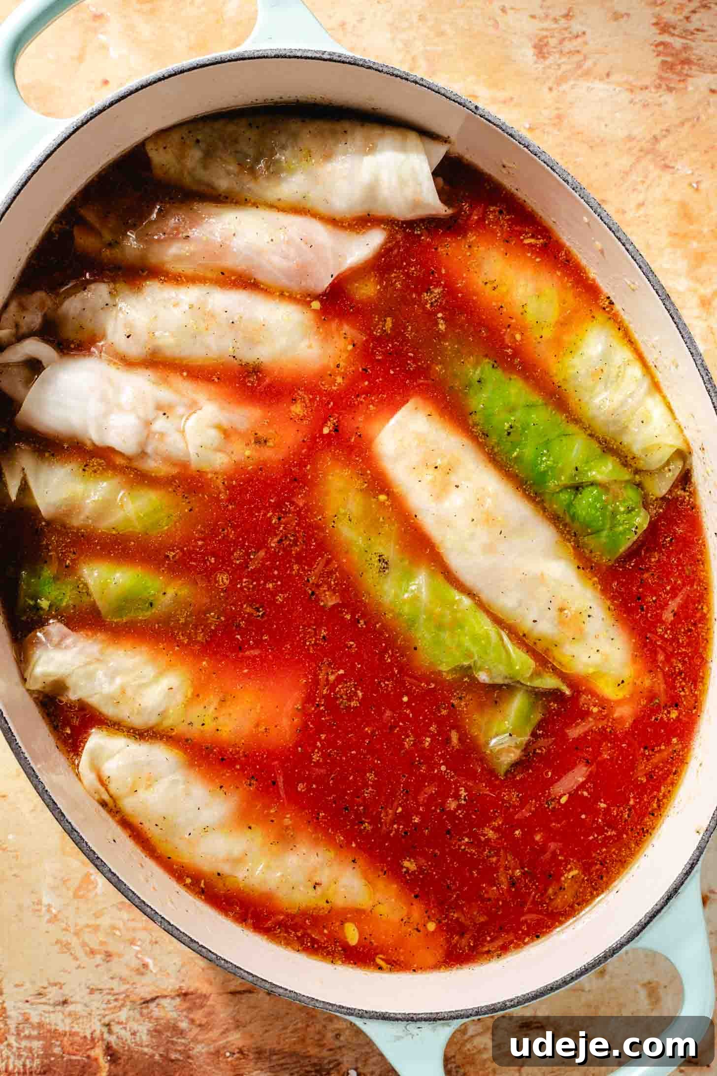 Irresistible Beef and Rice Cabbage Rolls 15 The blanched and stuffed cabbage leaves, artfully rolled and arranged in an oval light blue pot, are now completely covered with the seasoned broth, awaiting baking on a brown background.