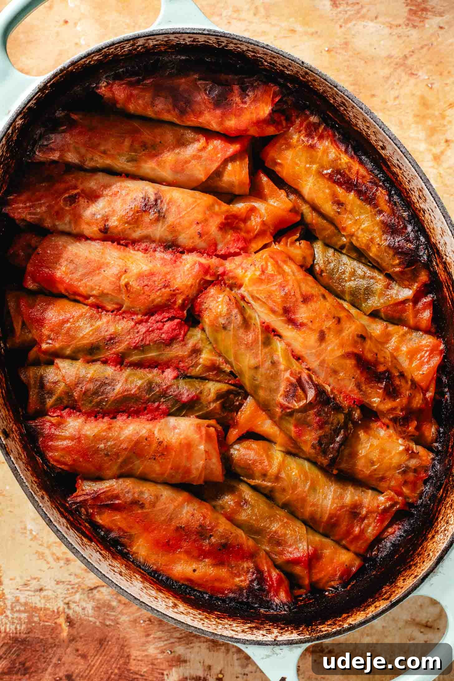 Irresistible Beef and Rice Cabbage Rolls 16 Beautifully baked cabbage rolls, glistening with broth, presented in a light blue pot on a rustic brown background, signifying a completed and delicious meal.