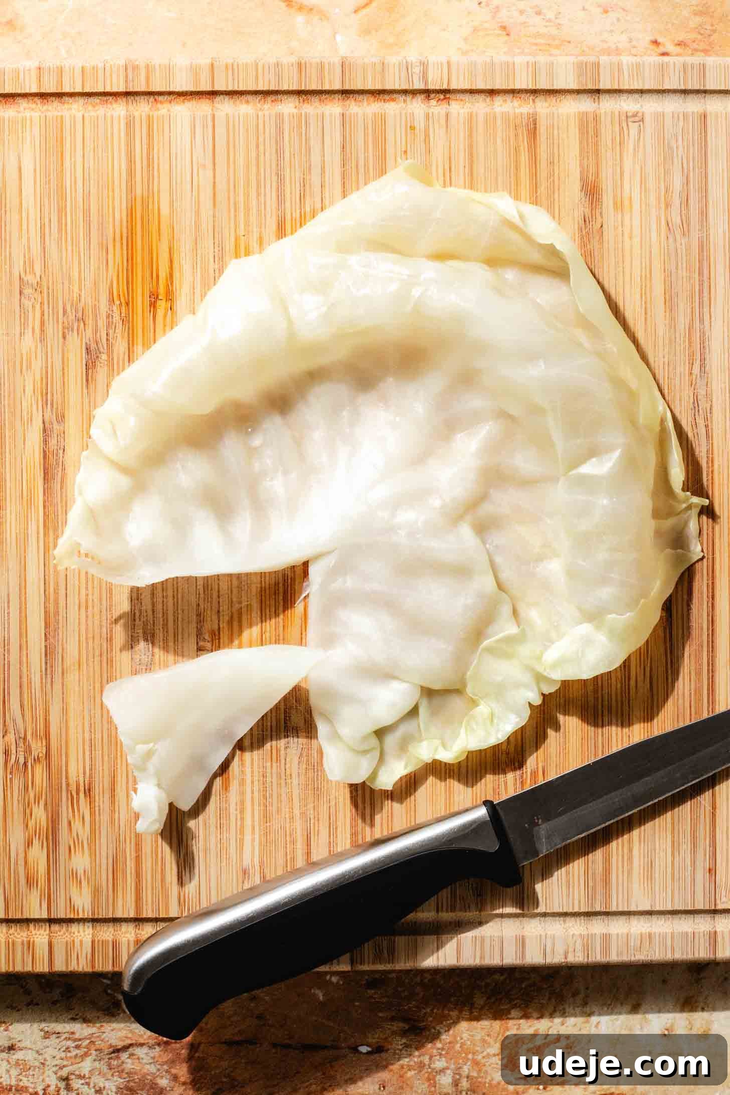 Irresistible Beef and Rice Cabbage Rolls 8 A blanched cabbage leaf laid flat on a light wooden cutting board, with its thick core expertly cut out and a knife resting beside it, indicating preparation for stuffing.