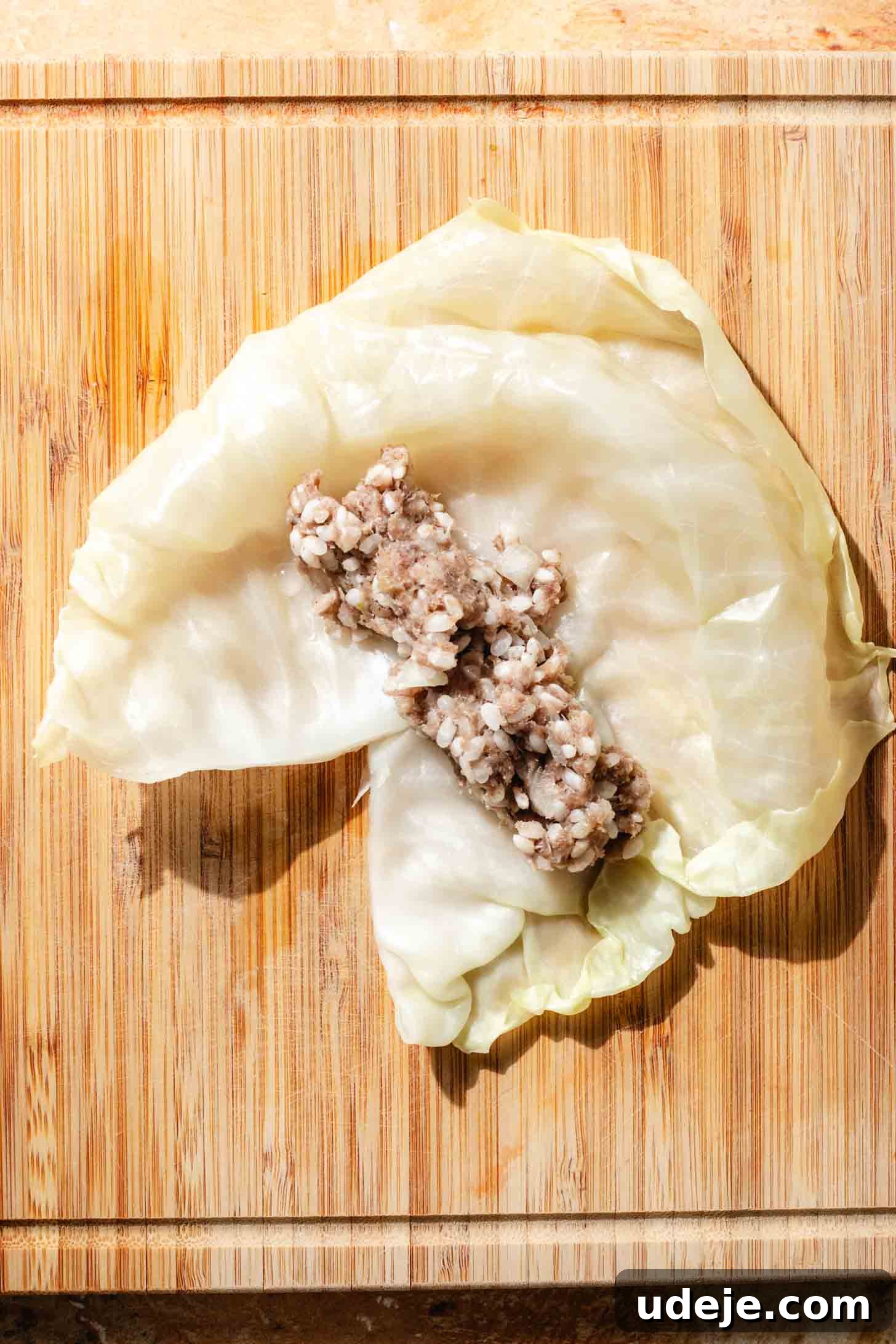 Irresistible Beef and Rice Cabbage Rolls 9 A blanched cabbage leaf with a perfectly shaped log of ground beef mixture placed at its center, ready for the rolling process on a light wooden background.