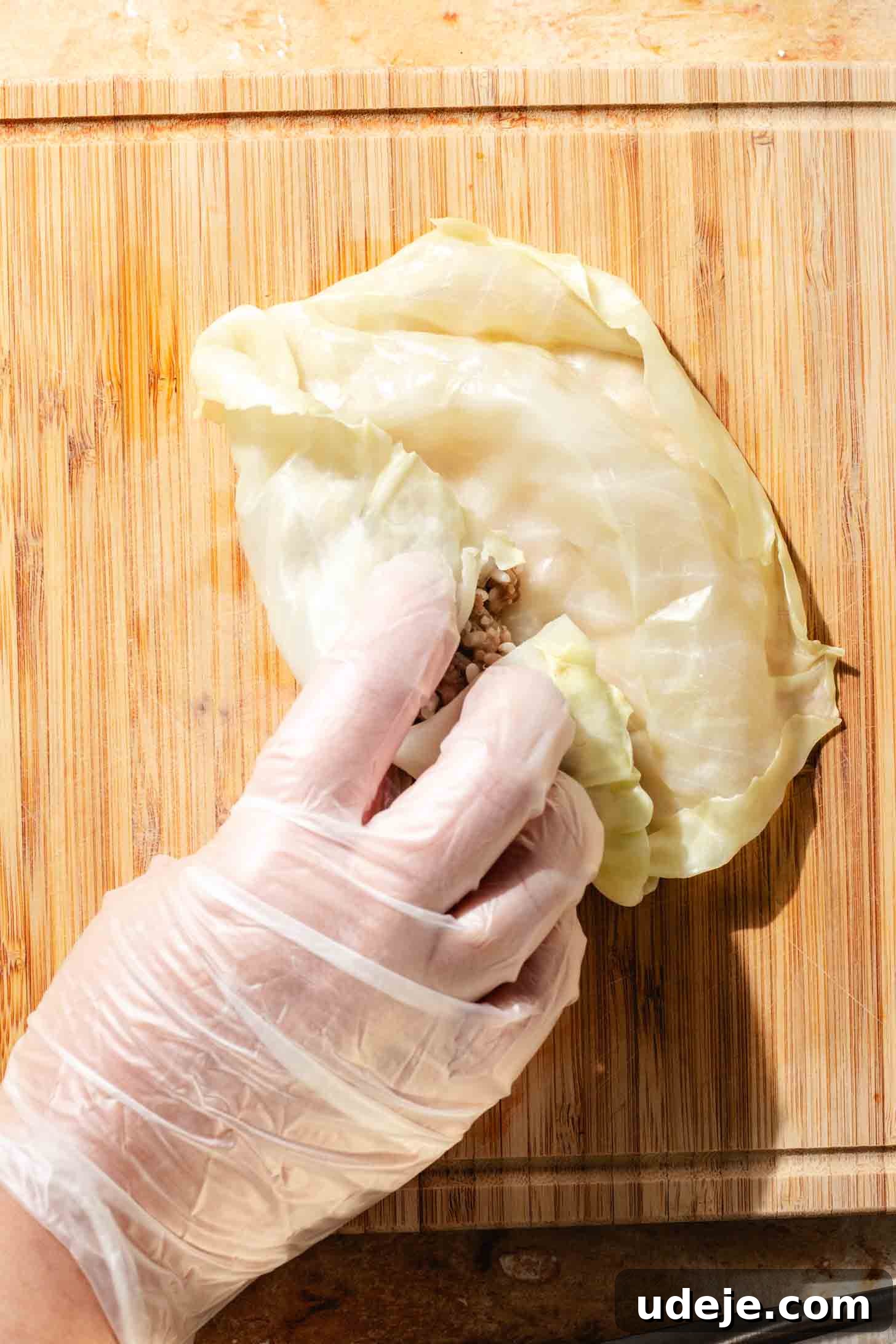 Irresistible Beef and Rice Cabbage Rolls 10 A gloved hand expertly rolling a blanched cabbage leaf over the ground beef mixture, forming a tight, compact roll on a light wooden background.