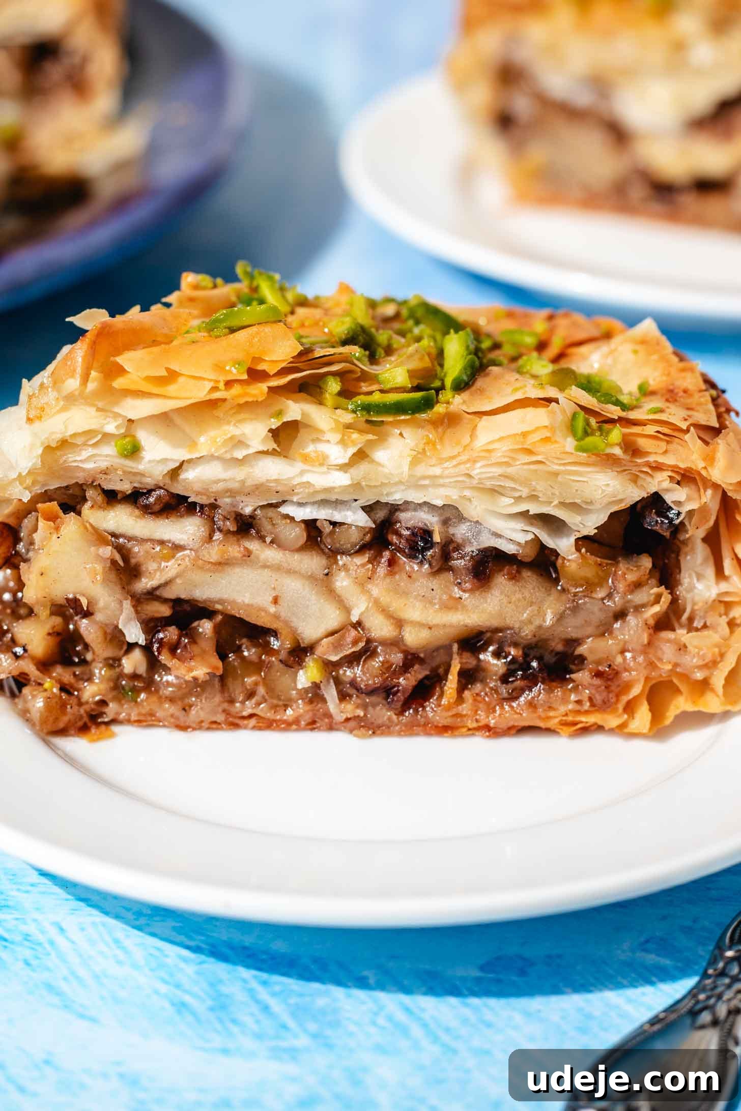 Apple Pie Meets Baklava 3 A close-up side view of a generous slice of Baklava Apple Pie on a white plate, highlighting its distinct layers of phyllo and apple filling.