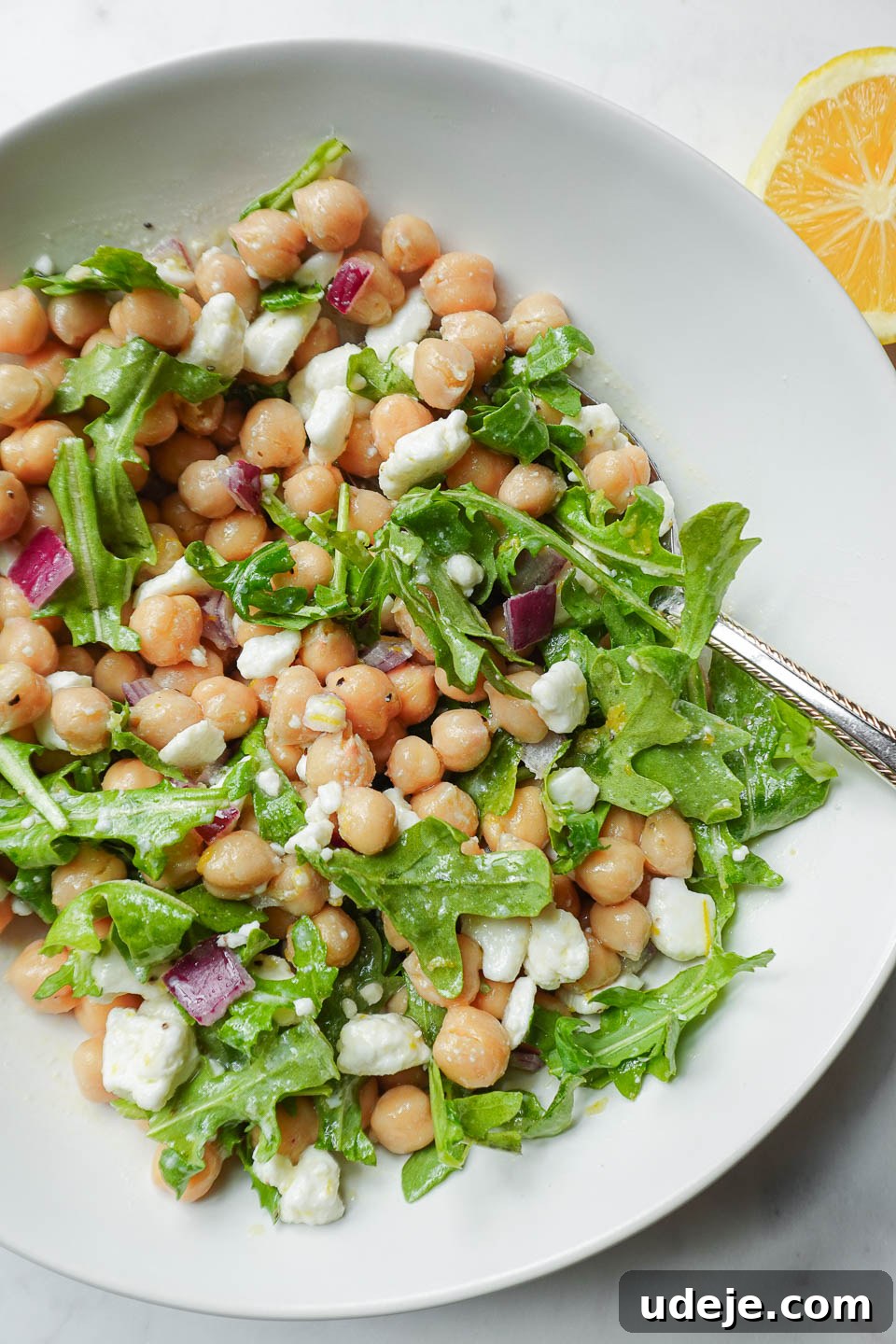 Vibrant Vegan Lemon Chickpea Salad 3 Overhead close-up of lemon chickpea salad, showcasing chickpeas, vegan feta, fresh arugula, and red onion perfectly coated in a luminous lemon dressing, ready to be enjoyed.
