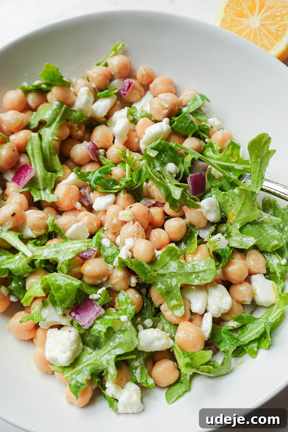 Vibrant Vegan Lemon Chickpea Salad 5 Close-up view of a spoon scooping up a portion of vegan chickpea salad, highlighting the texture of feta, arugula, and chickpeas perfectly coated in the bright lemon vinaigrette.