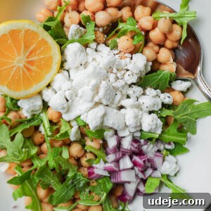 Overhead view of lemon chickpea salad with chickpeas, vegan feta, arugula, red onion, and lemon wedge, presented in a recipe card format.