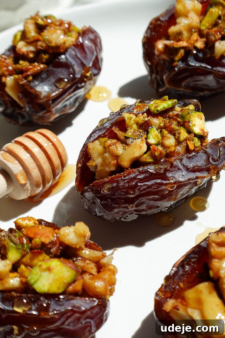 Gourmet Baklava-Filled Dates 5 Baklava dates filled with pistachios, walnuts, and cinnamon arranged on a white plate with a honey comb.