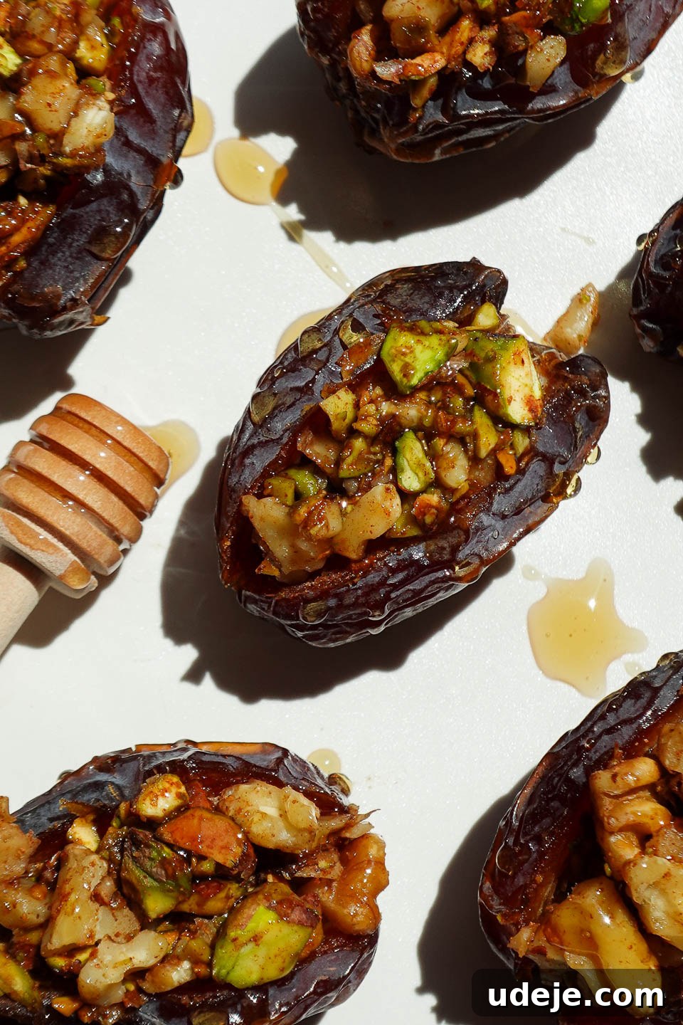 Gourmet Baklava-Filled Dates 6 Baklava stuffed dates filled with pistachios, walnuts, and cinnamon arranged on a white plate.