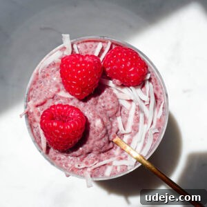 jar of raspberry chia pudding topped with fresh berries and coconut flakes on a white background